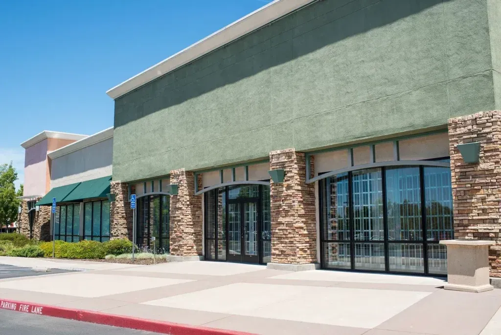 Strip mall storefronts with green awnings and stone pillars on a sunny day