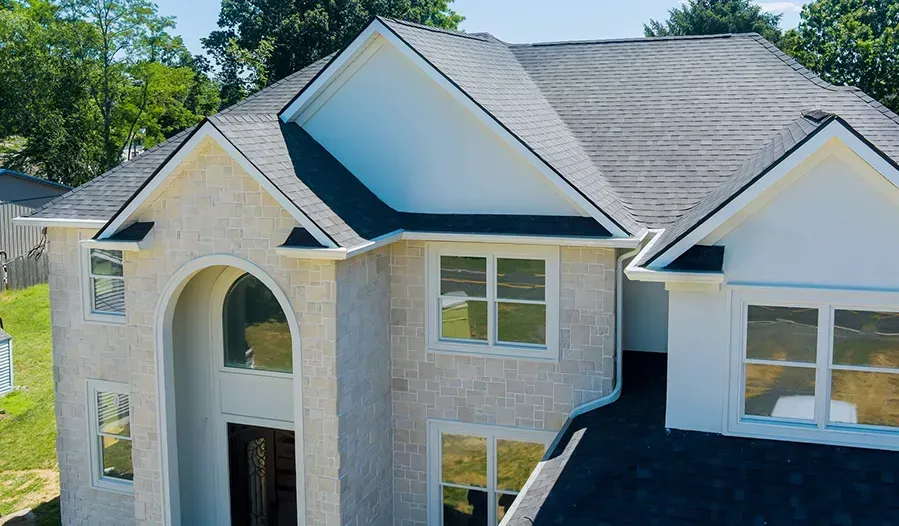 Aerial view of a suburban house with a light brick exterior and gray shingled roof