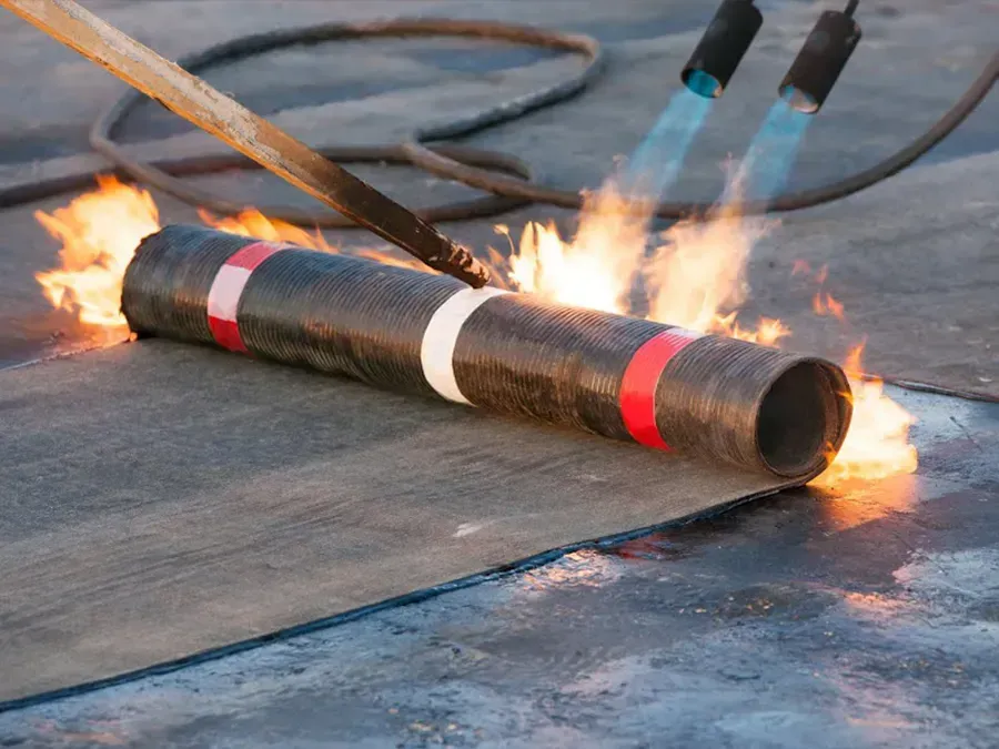 Worker torch-cutting a black pipe with red and white bands, sparks and flames on an outdoor surface