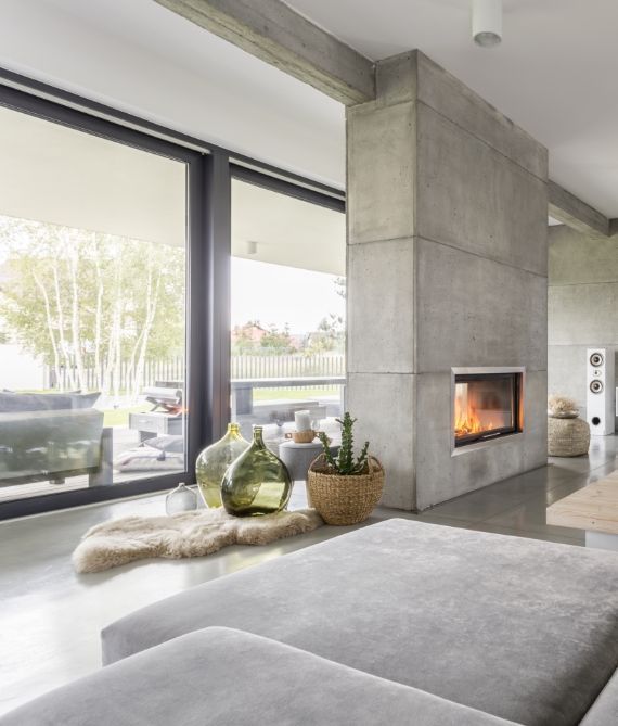 Modern living room with floor-to-ceiling windows, concrete fireplace, and low sofa with decorative vases.
