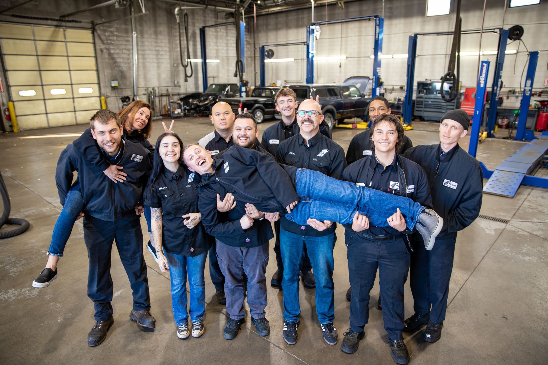 Group of auto shop employees, laughing, holding and carrying each other in a garage. | 5th Gear Automotive