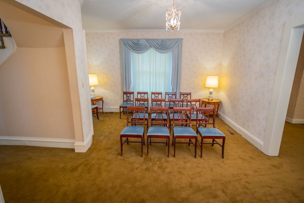 Interior of a room with chairs arranged in rows facing a window, brown carpet, soft lighting.