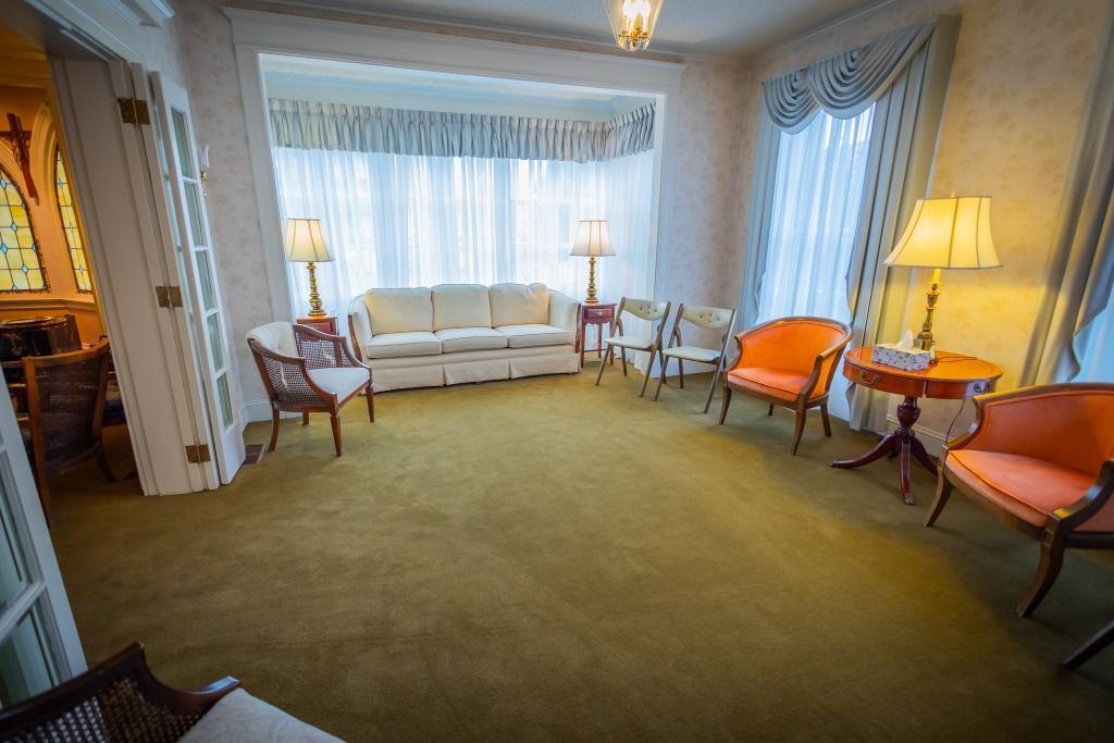 A waiting room with chairs, sofa, lamps, and a large window with sheer curtains.
