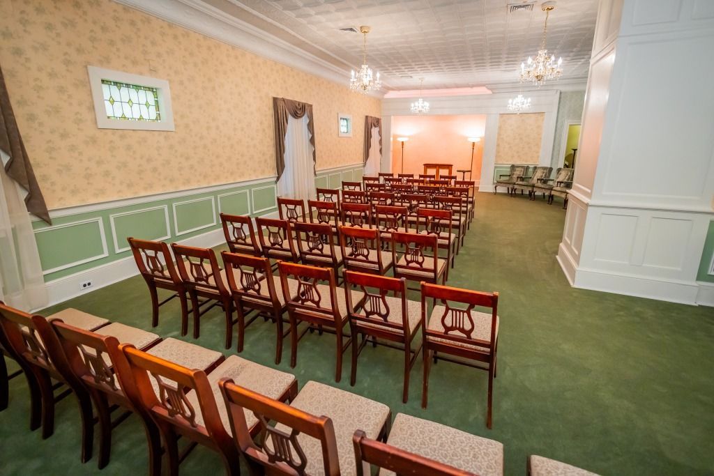 Rows of wooden chairs face an altar in a decorated room with patterned wallpaper.