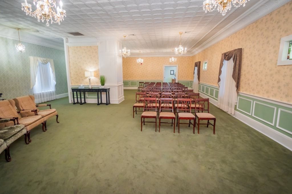 An empty room set up for a ceremony, rows of chairs face a center aisle. A wedding dress hangs on the right wall.