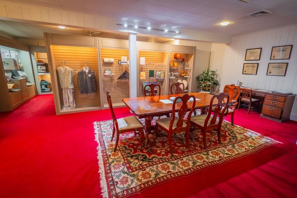 Museum display room with red carpet, glass cases, and a dining table.