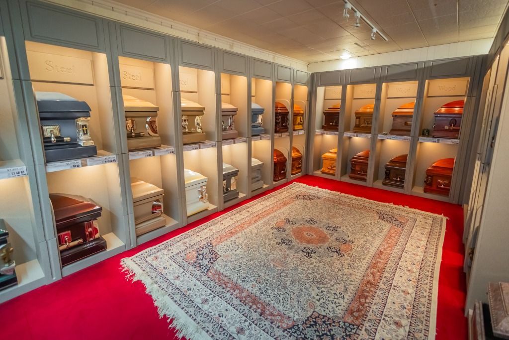Room displaying numerous ornate, lit caskets on shelves, with a patterned rug on a red carpet.