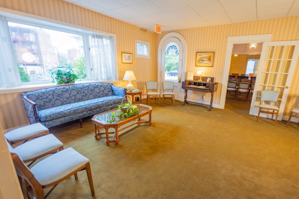 Funeral home waiting room with a blue floral sofa, chairs, and a coffee table, with yellow wallpaper and carpet.