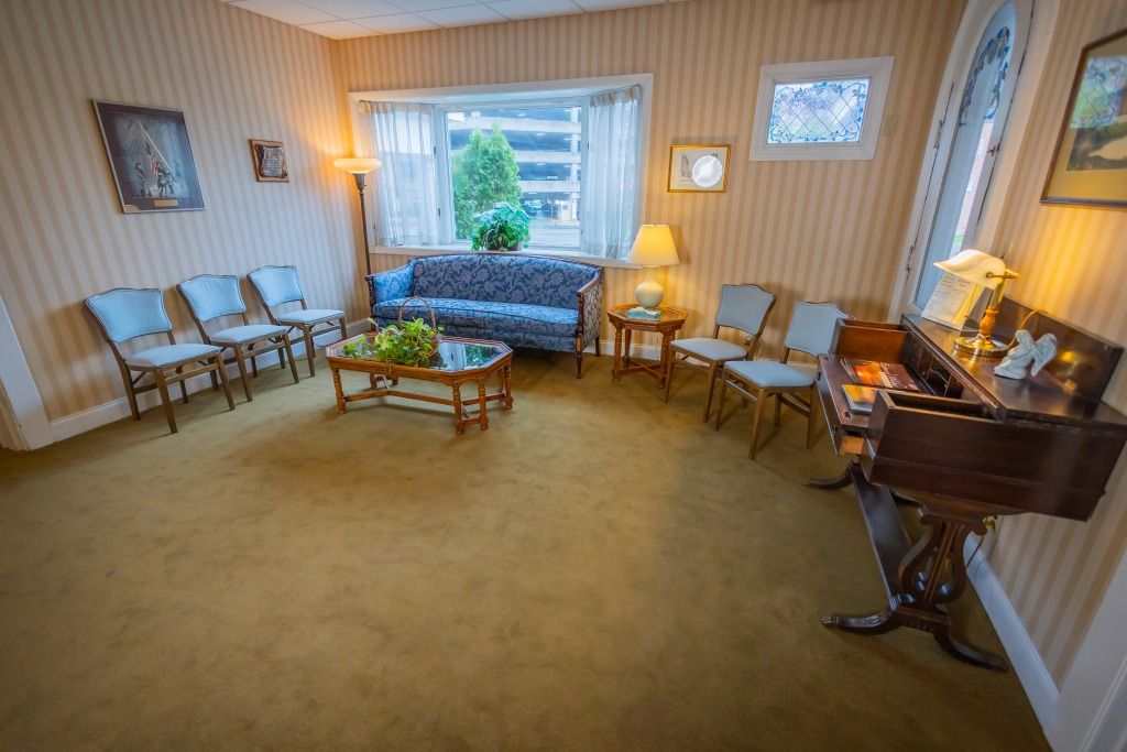 Waiting room with chairs, sofa, and a piano. Gold carpet, striped wallpaper, and a window with a view.