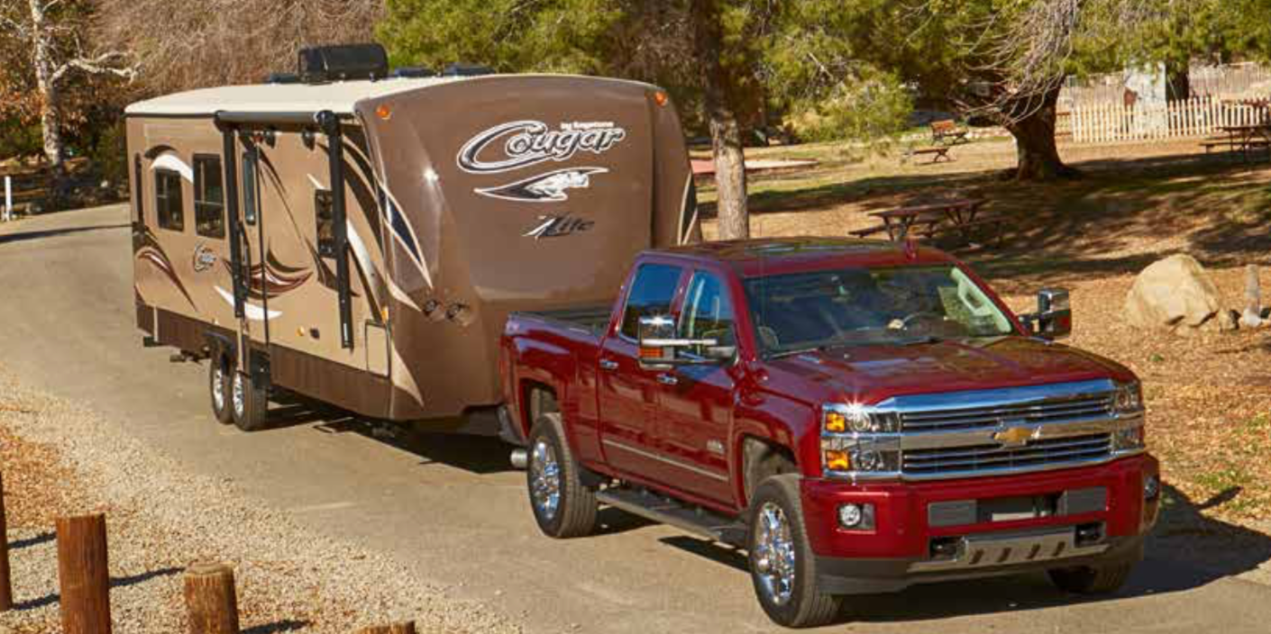 A red truck is towing a trailer down a dirt road.