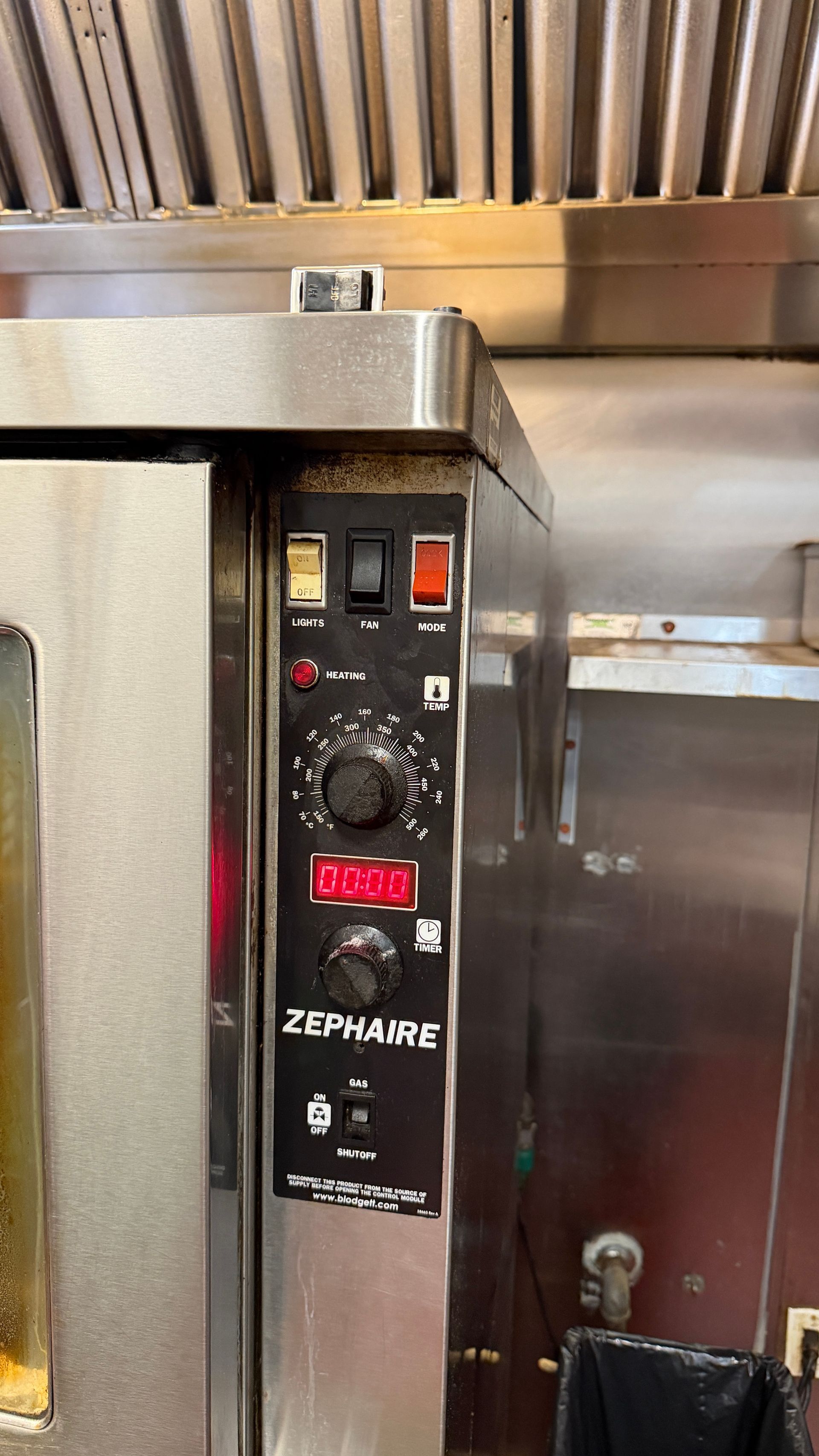 Stainless steel commercial oven with control panel under kitchen hood