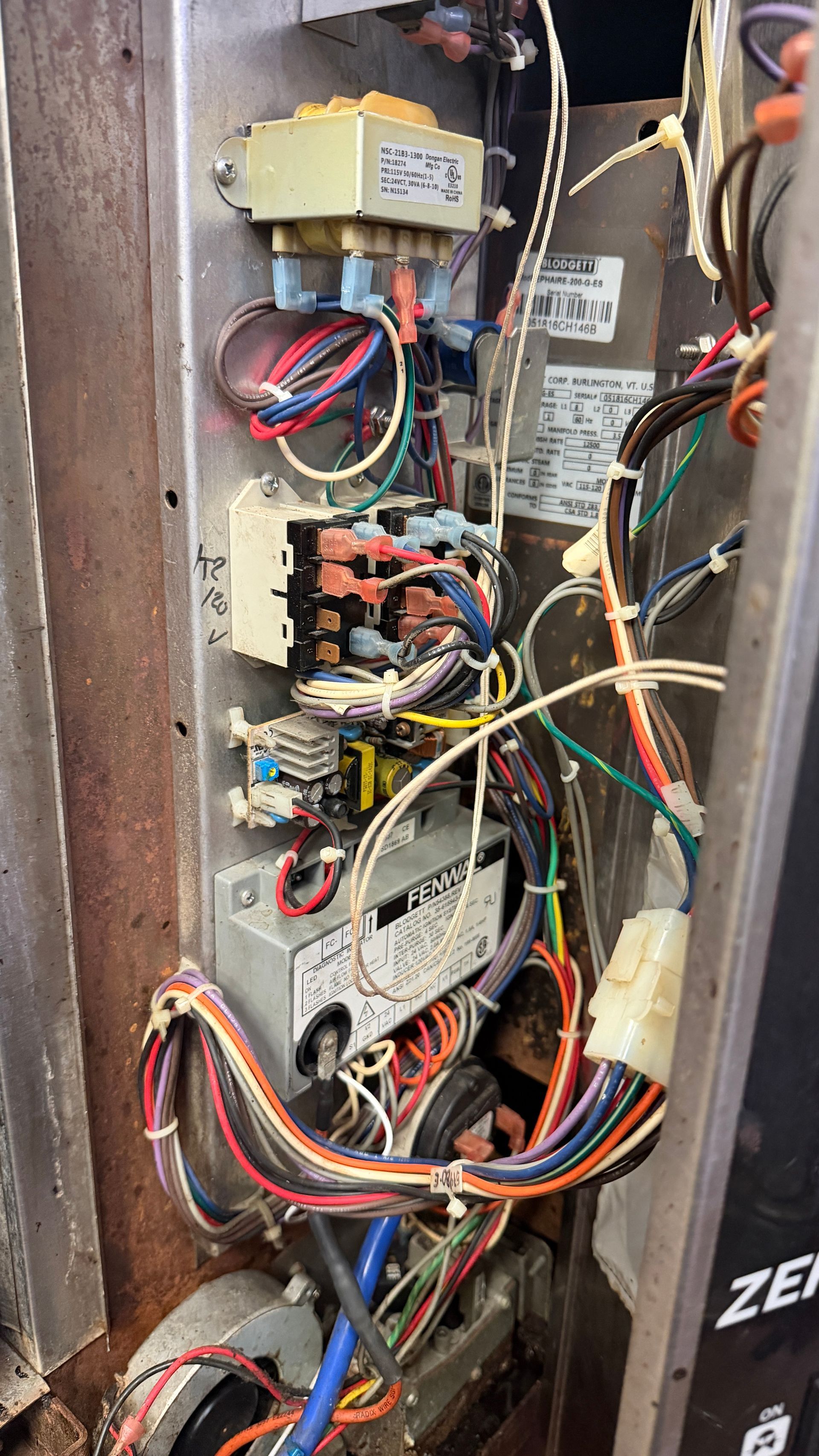 Open electrical control panel with tangled multicolored wires and circuit components.