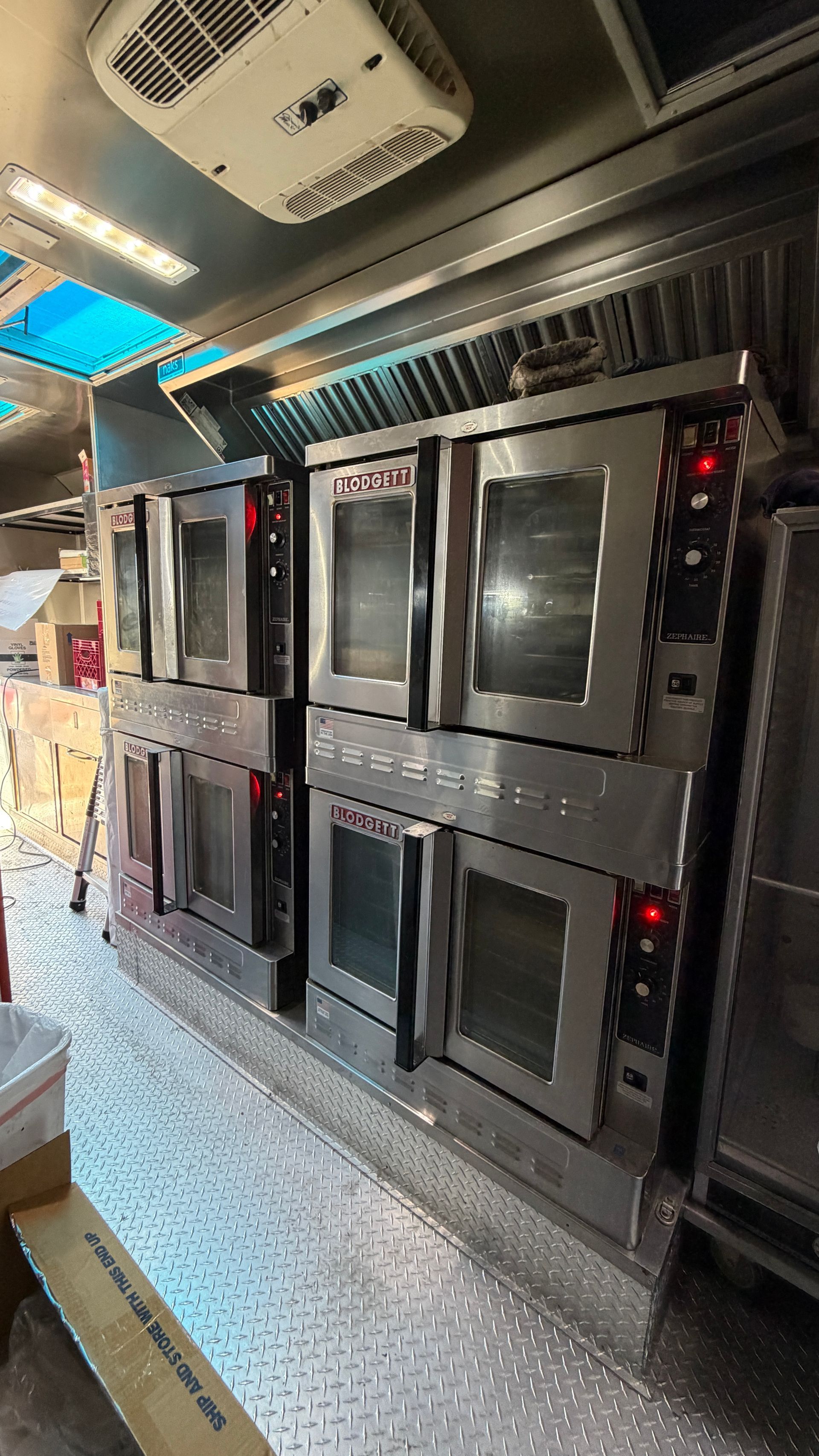 Row of black wall-mounted ovens or incubators inside a stainless steel industrial kitchen trailer