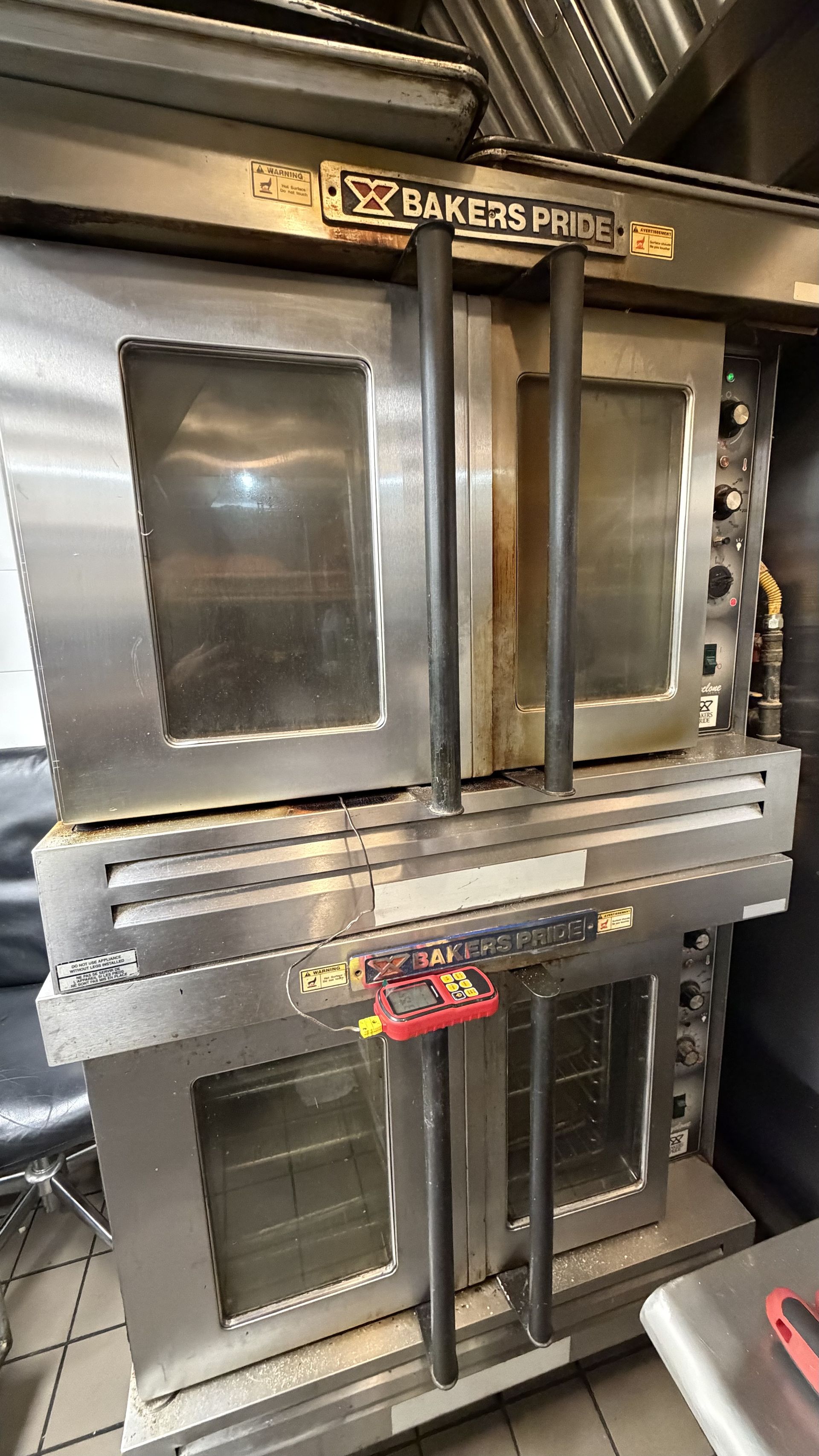 Stacked stainless steel bakery ovens in a kitchen, with glass doors and a bakery sign.