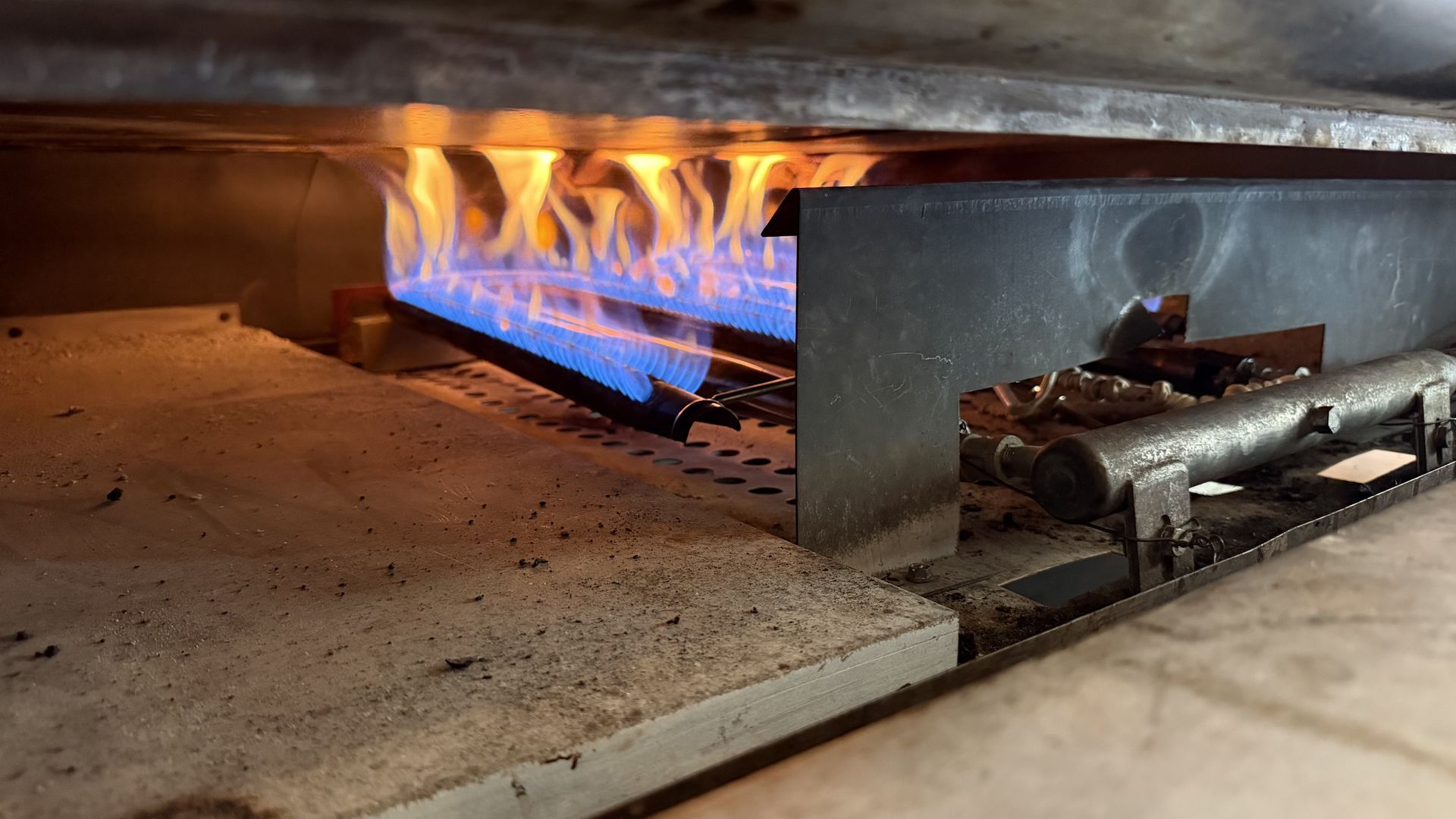 Blue and orange flames heating a metal industrial furnace on a concrete floor