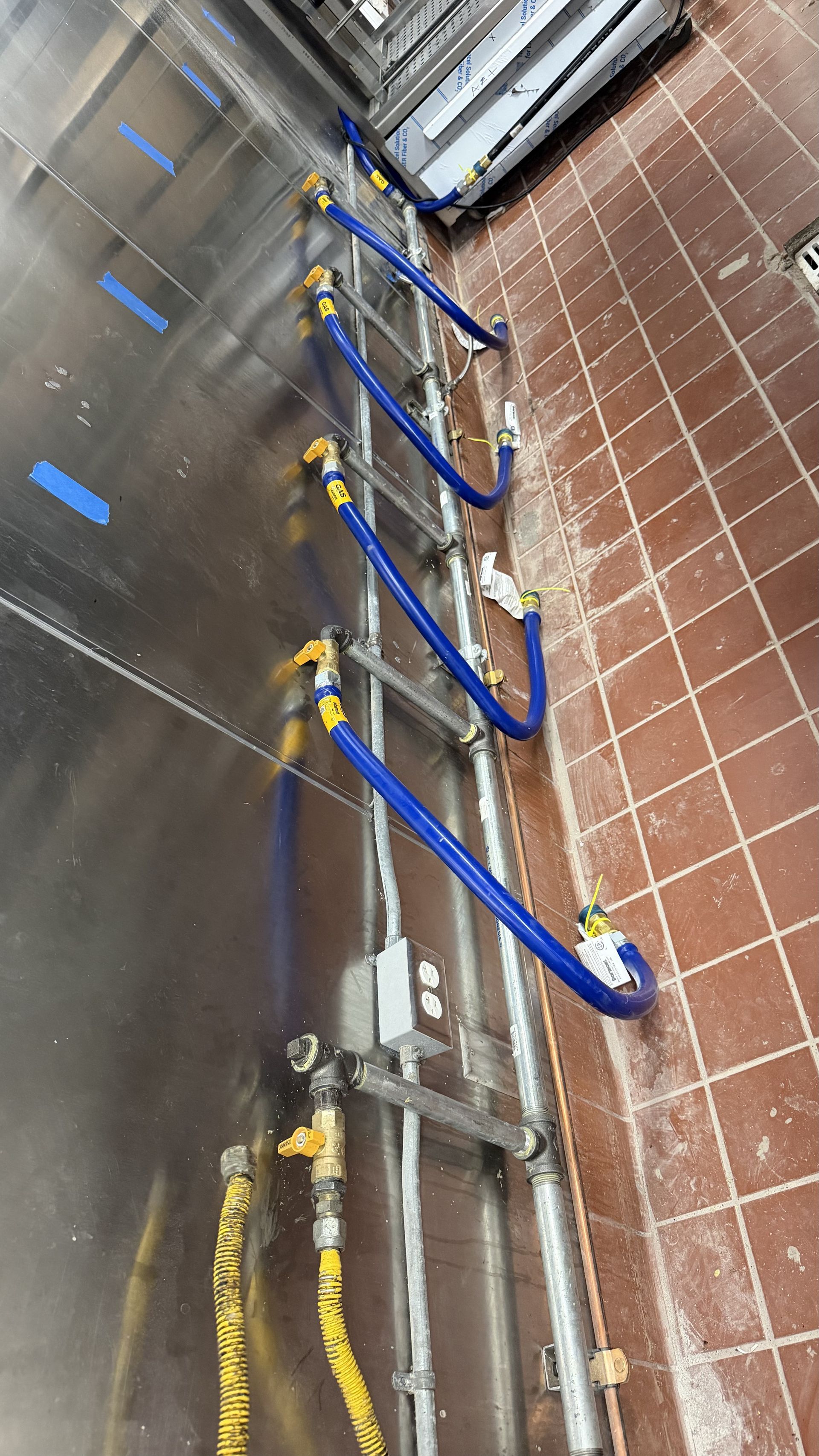 Blue hoses and metal pipes lined along a tiled wall in an industrial utility area.