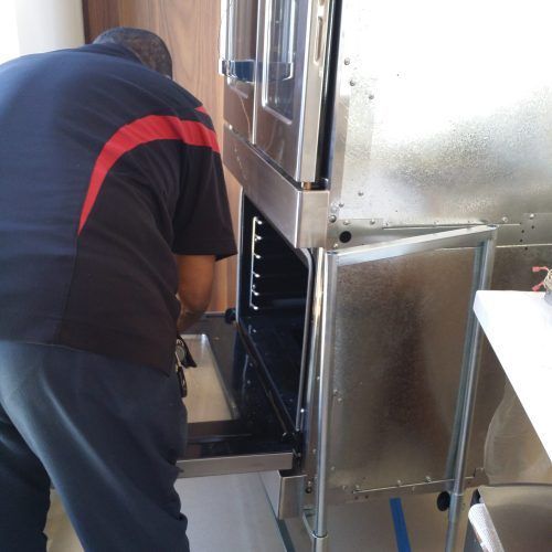 Person loading an industrial oven or dishwasher, with the door open in a kitchen area