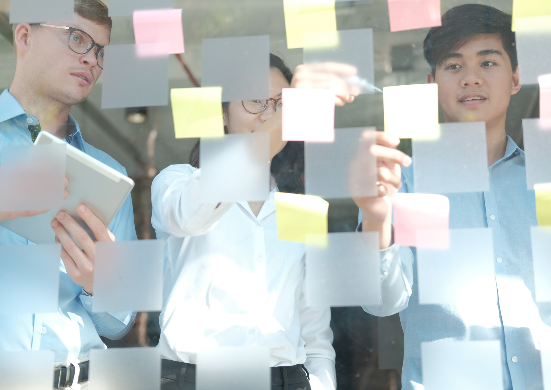 Colleagues arranging sticky notes on a glass wall during a planning session