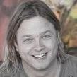 A man with long hair is smiling in a black and white photo.