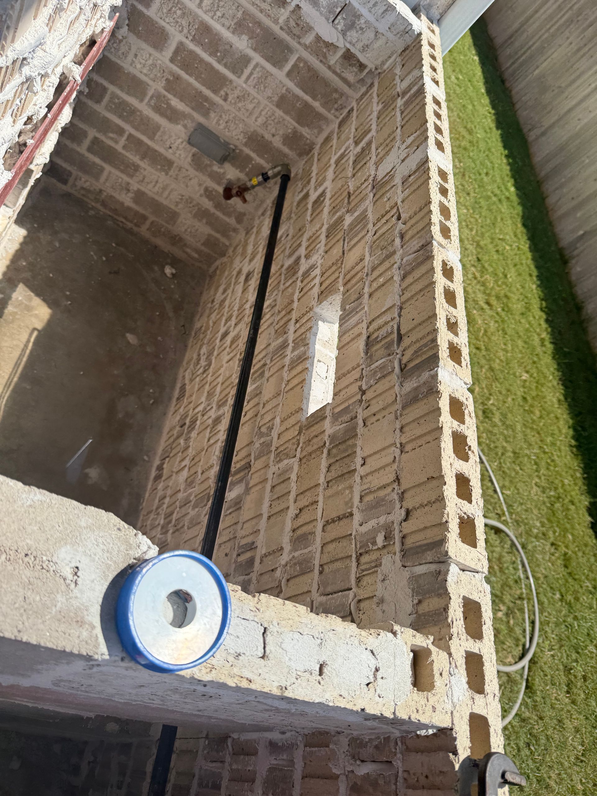 Brick-lined outdoor sink area with a blue bowl on the ledge and a black hose on the wall.