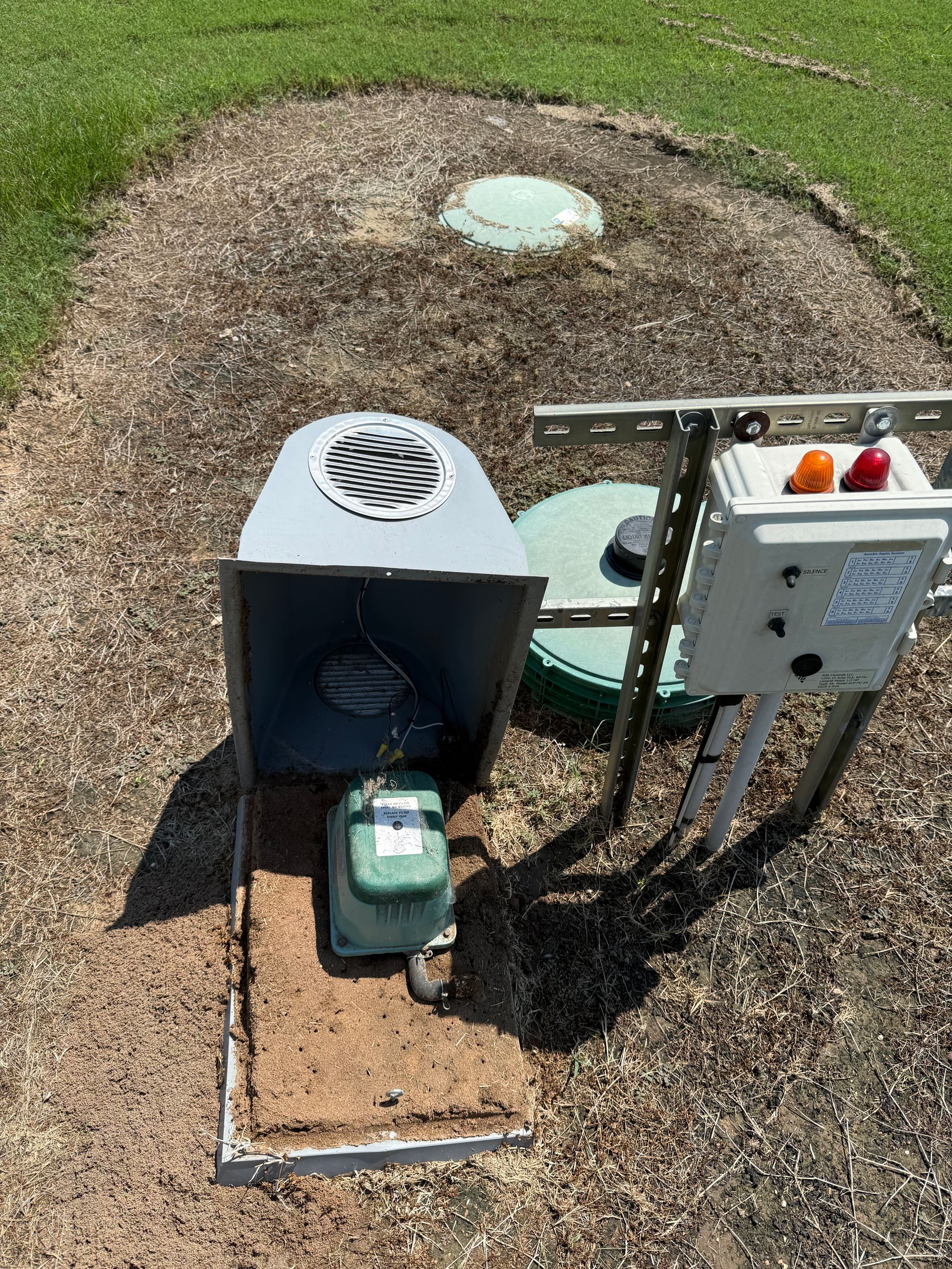 Outdoor utility equipment with control box and gauge mounted beside a small green tank in a grassy area