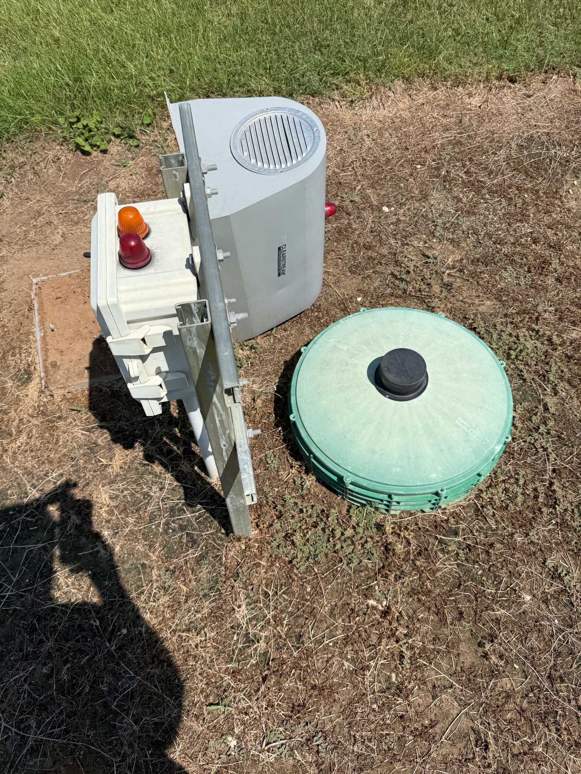 Outdoor utility equipment and green round cover on dry grass, with a white cabinet and beacon light.