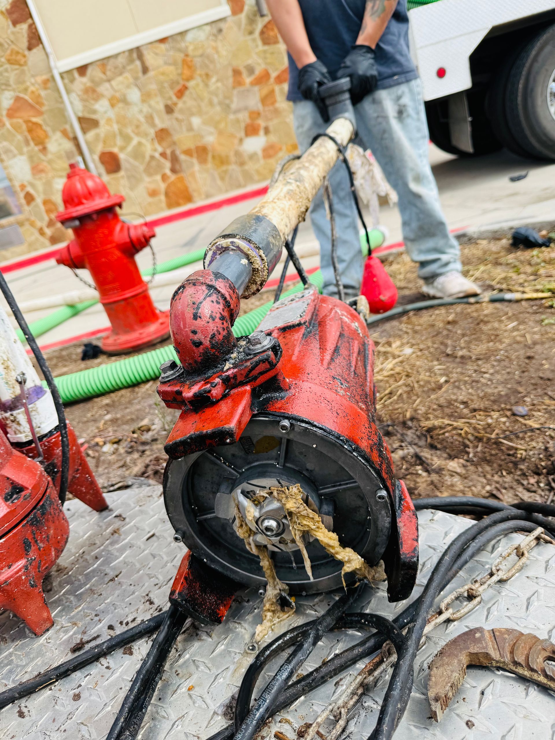 Damaged red fire hose pump on wet pavement with worker standing nearby and fire hydrant behind it