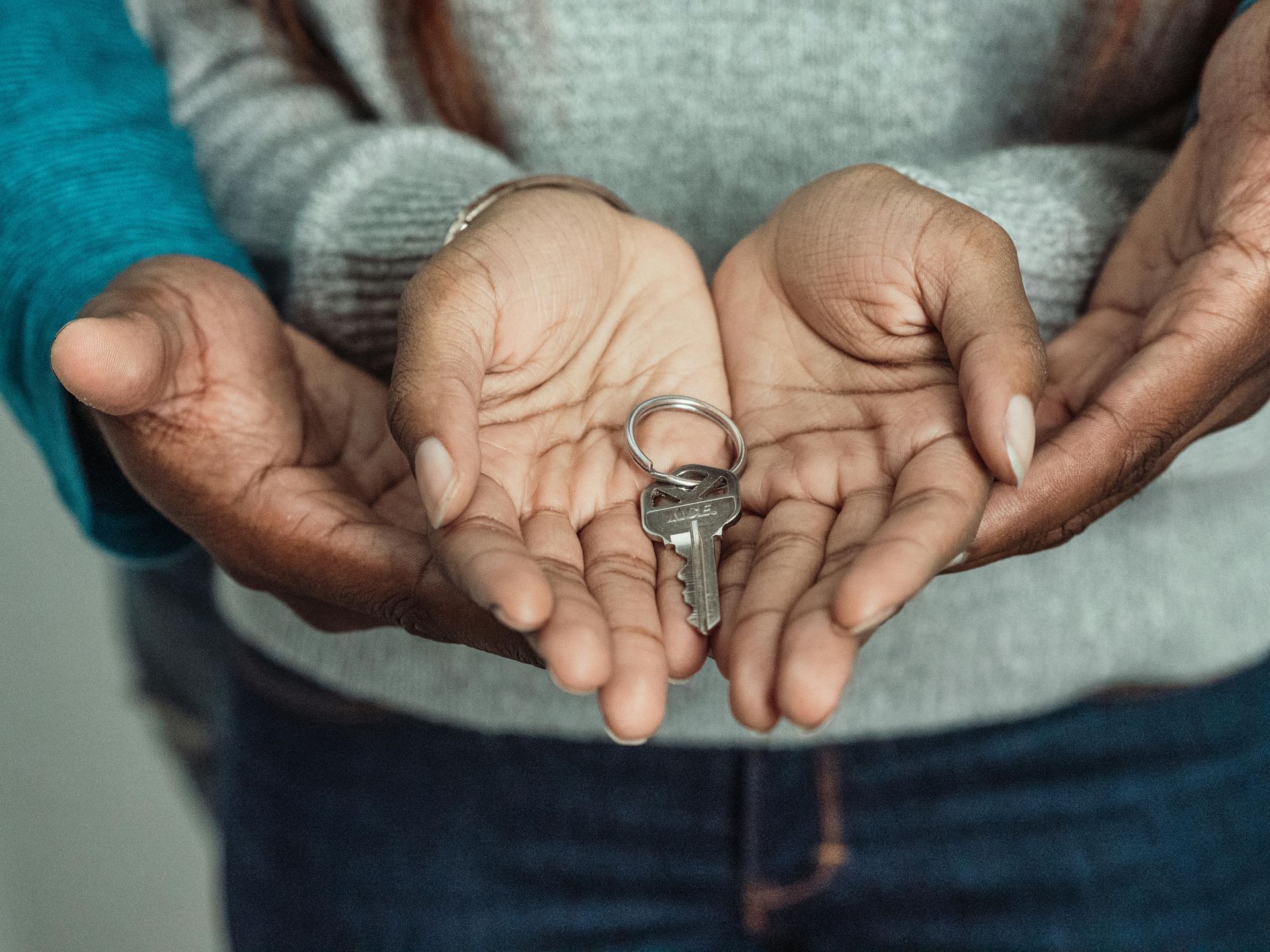 Hands holding a small key against a person’s jeans, symbolizing home or security