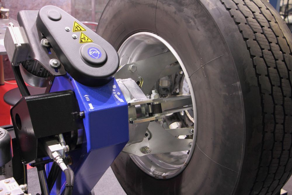 A large truck tire being balanced on a blue machine; gray metal arms extend toward the tire.