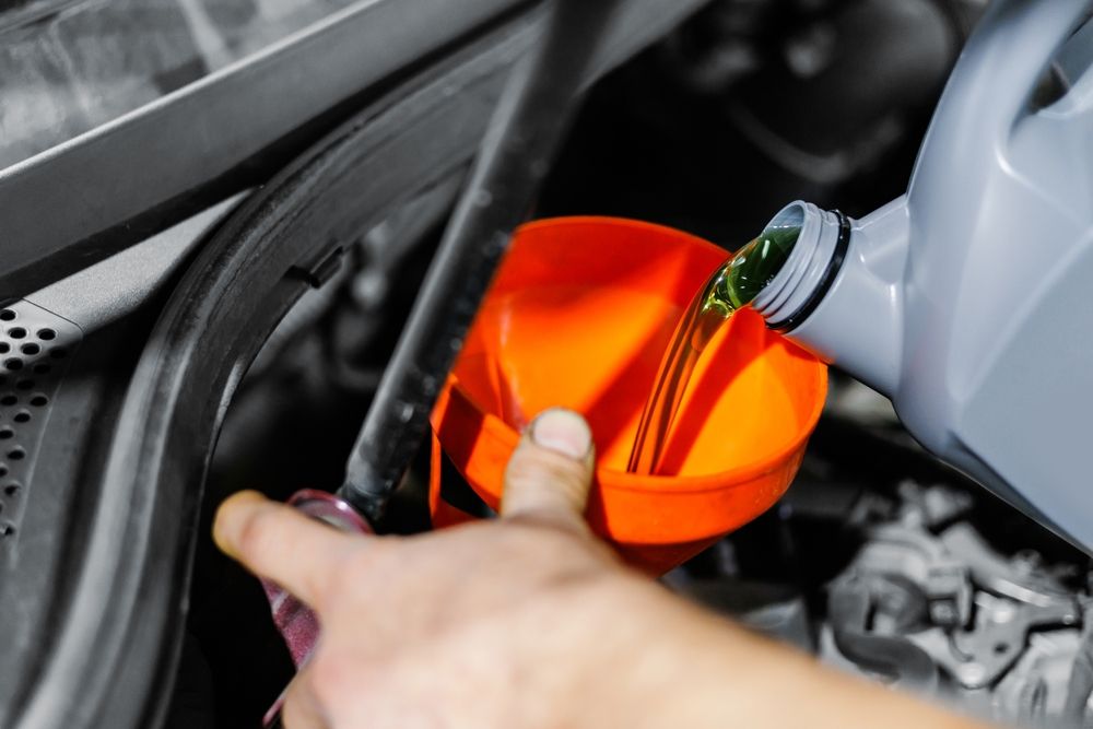 Person pouring oil into a car engine using a funnel.