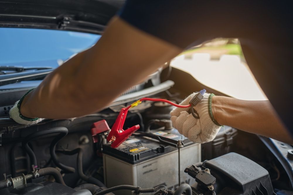 Person connecting jumper cables to a car battery under the hood.