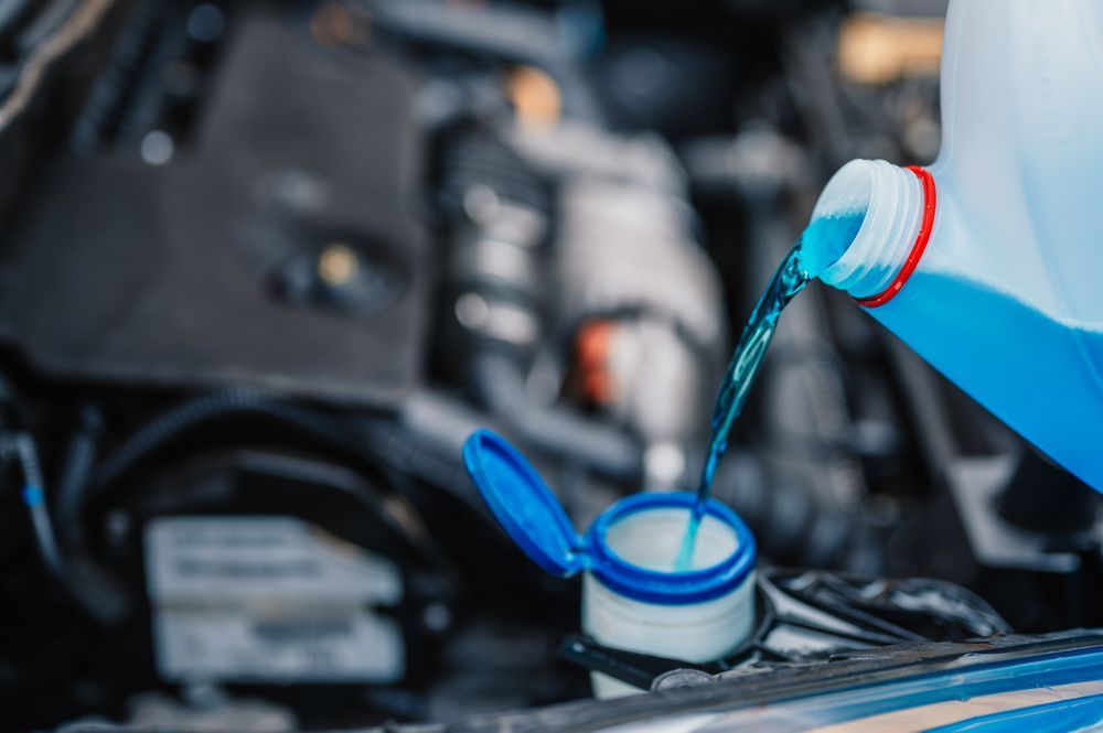 Blue windshield washer fluid being poured into a car's reservoir.