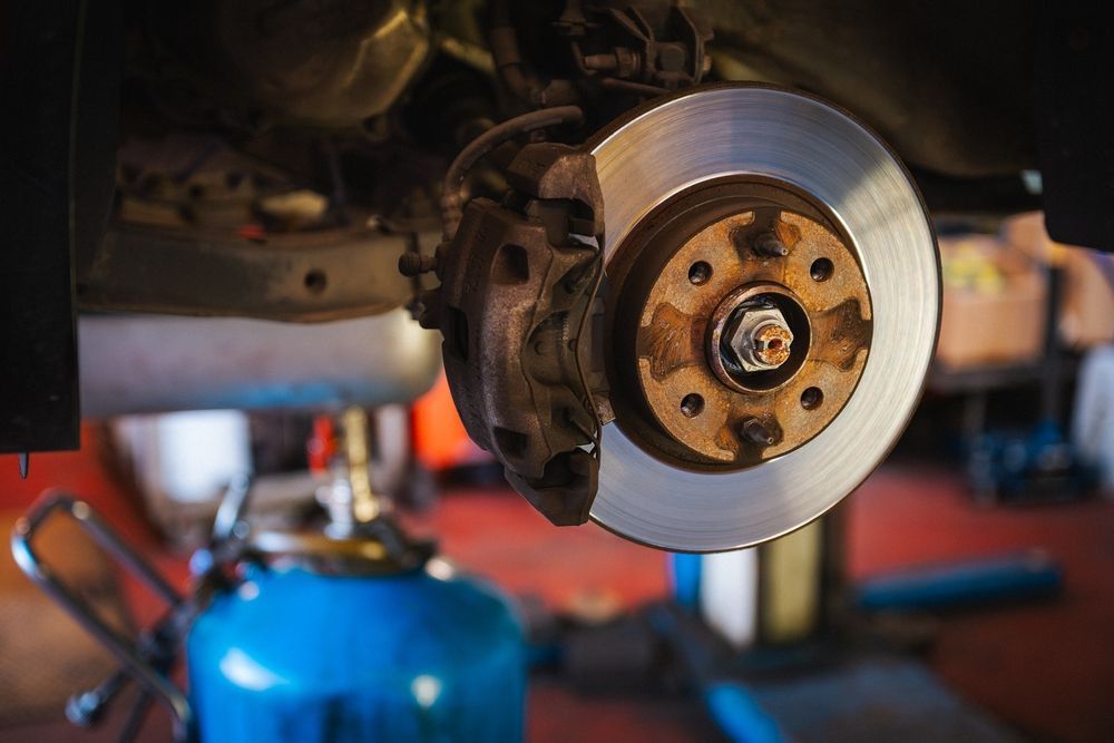 Car brake disc and caliper in a repair shop setting.