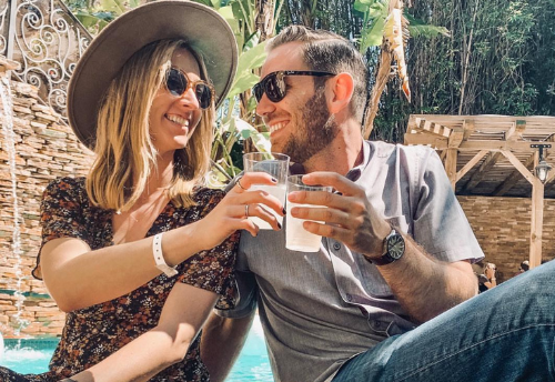 A man and a woman are sitting next to each other toasting with drinks.