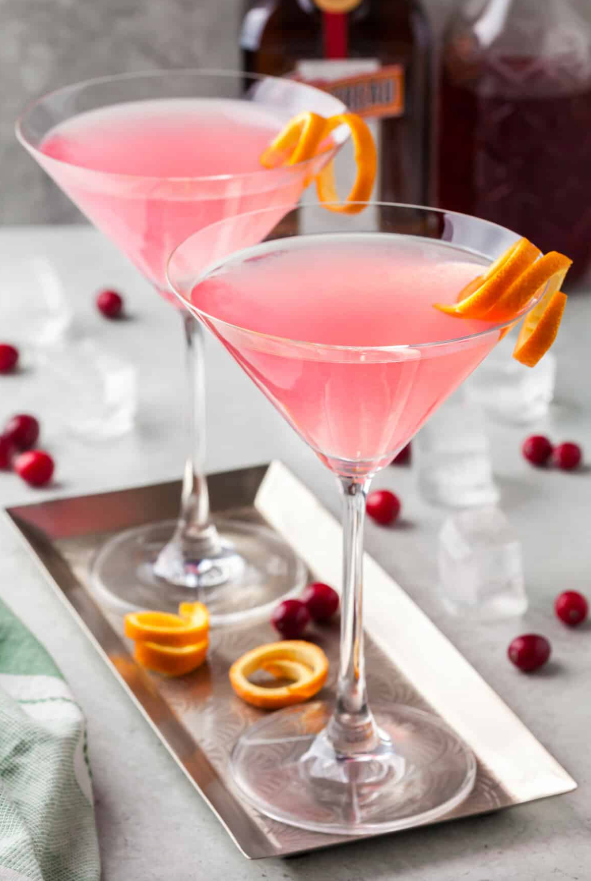 Two martini glasses filled with pink liquid and orange peel on a tray.
