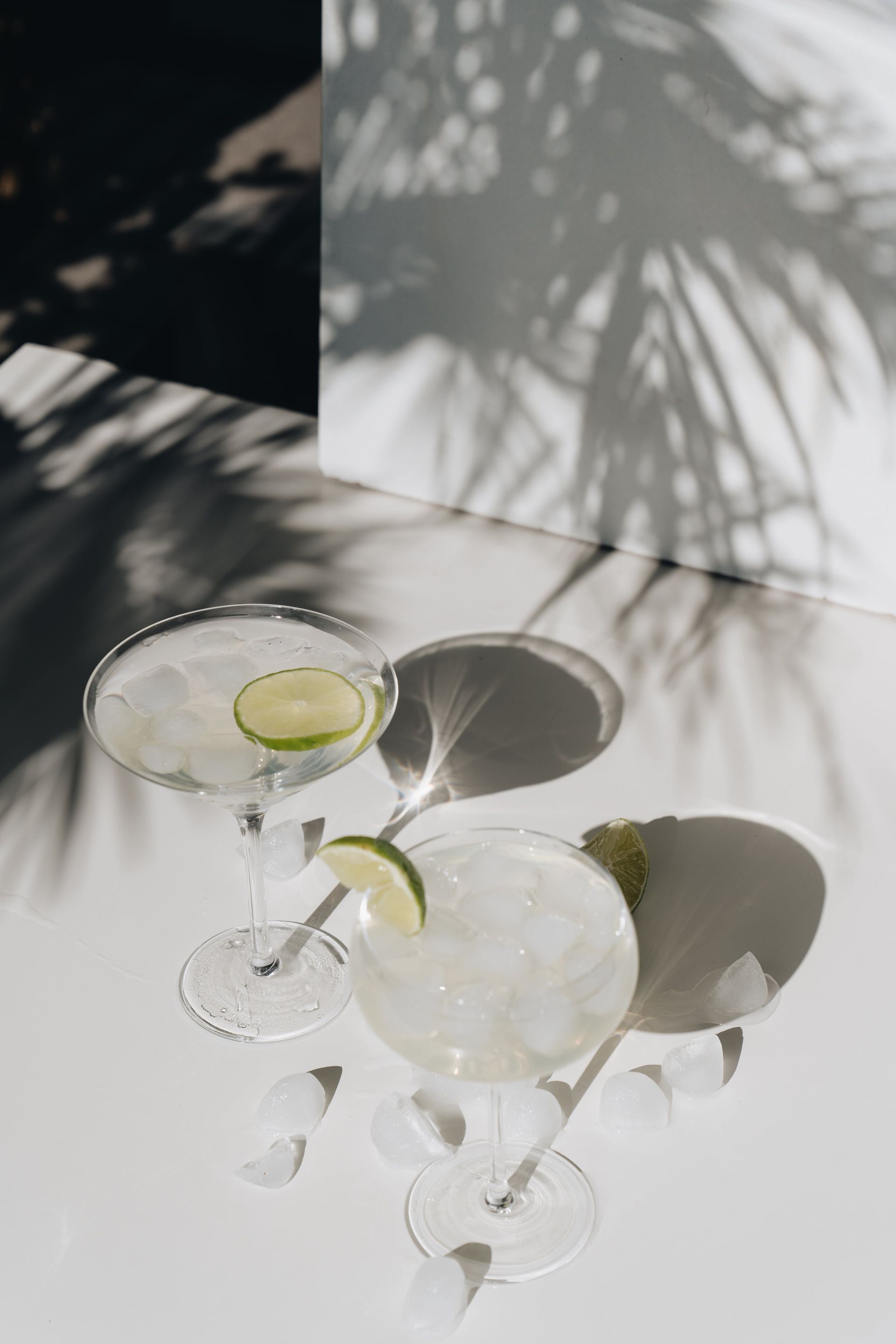 Two martini glasses with lime slices on a white table.