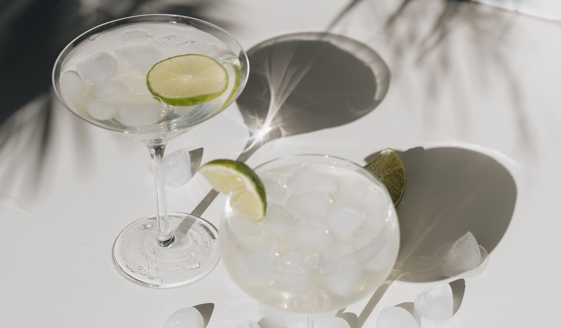 Two martini glasses with ice and lime slices on a table.