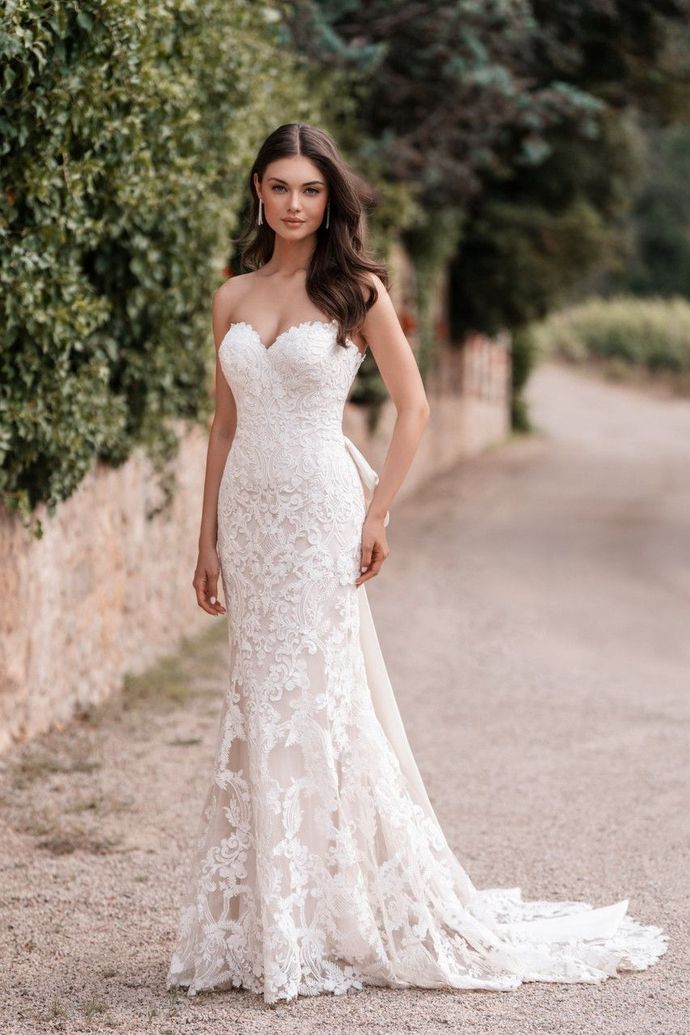 A woman in a white lace wedding dress is standing on a dirt road.
