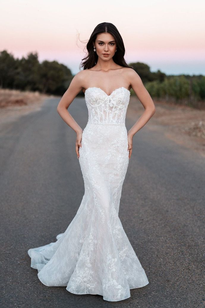 A woman in a white wedding dress is standing on a road.