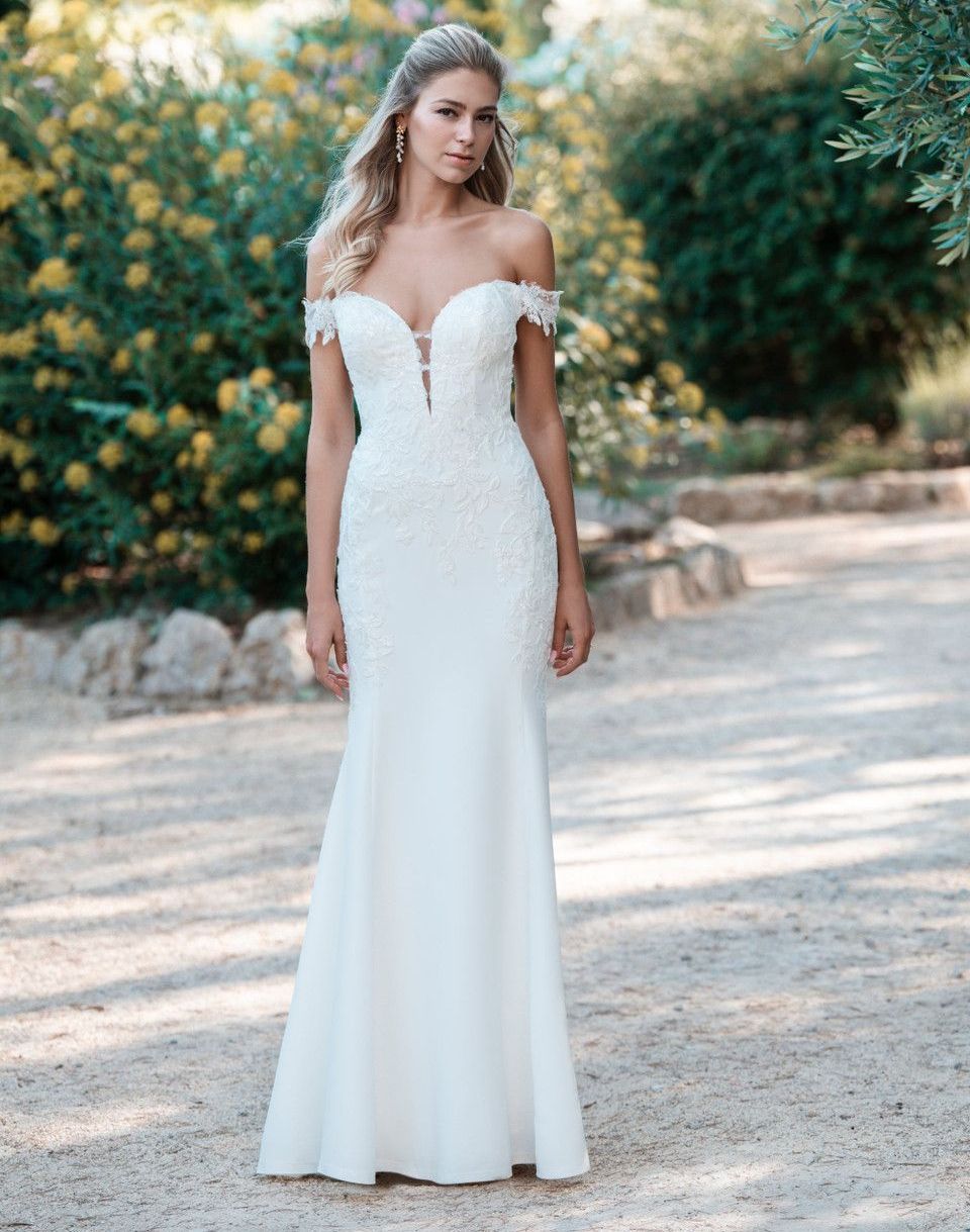 A woman in a white wedding dress is standing on a gravel road.