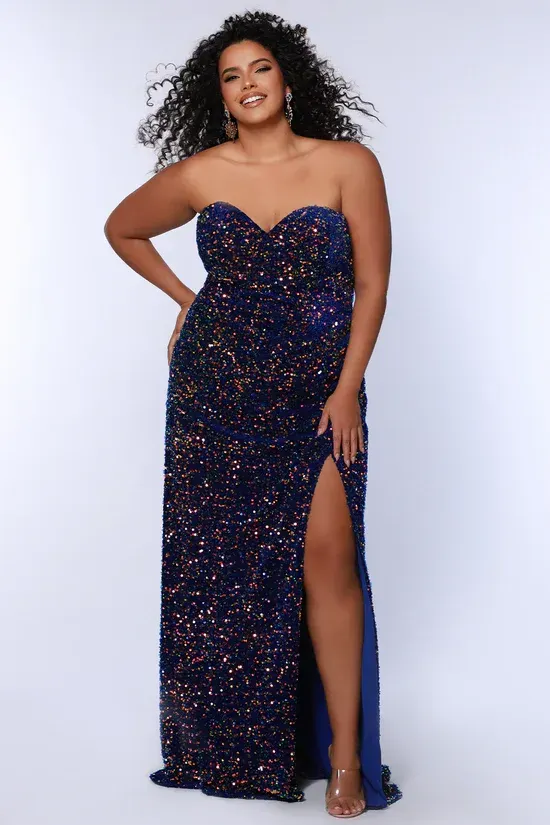 A plus size model is wearing a strapless blue sequined dress with a high slit.