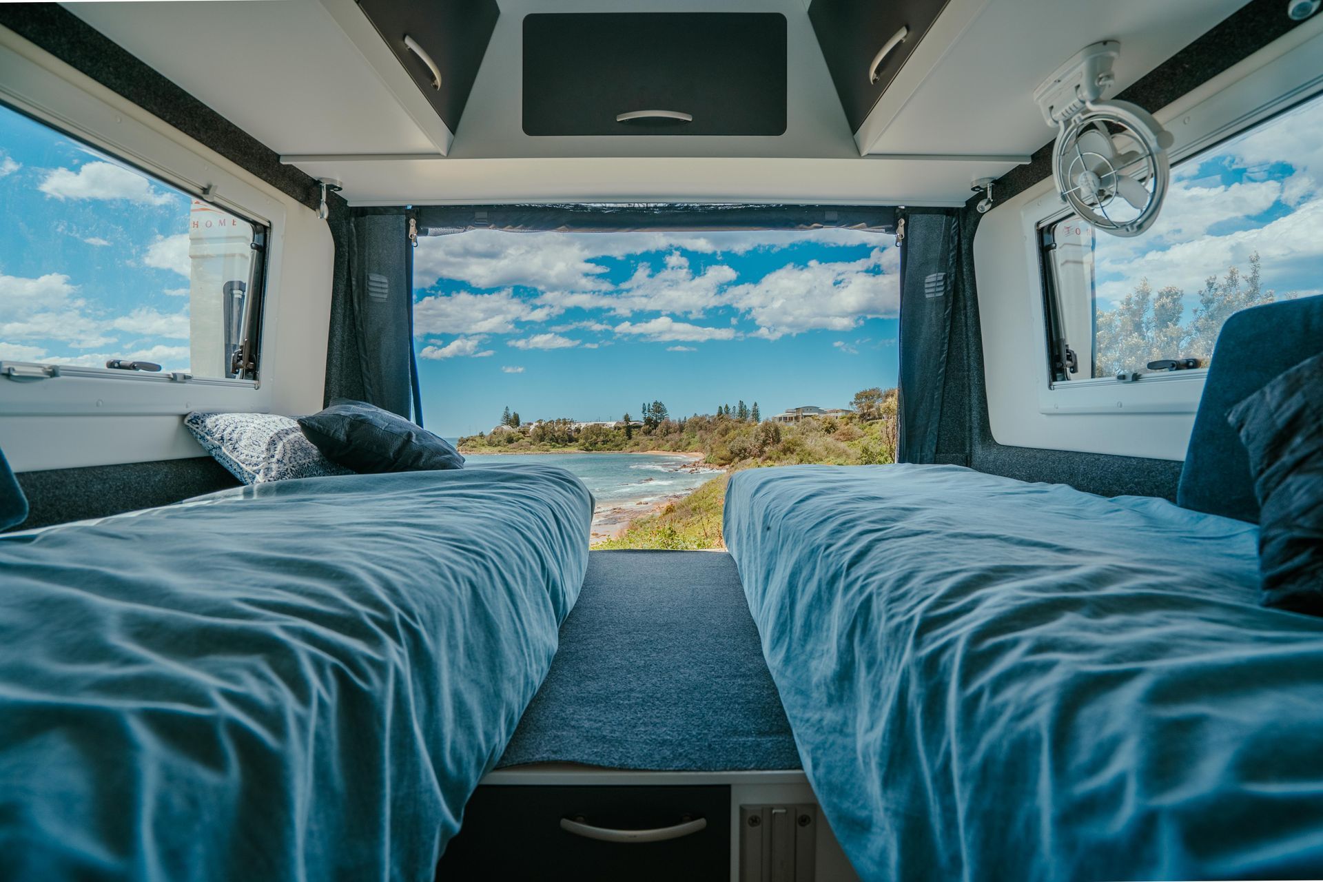 Inside campervan with two beds facing open window overlooking beach — Coastal Mattress' Direct in Brisbane, QLD