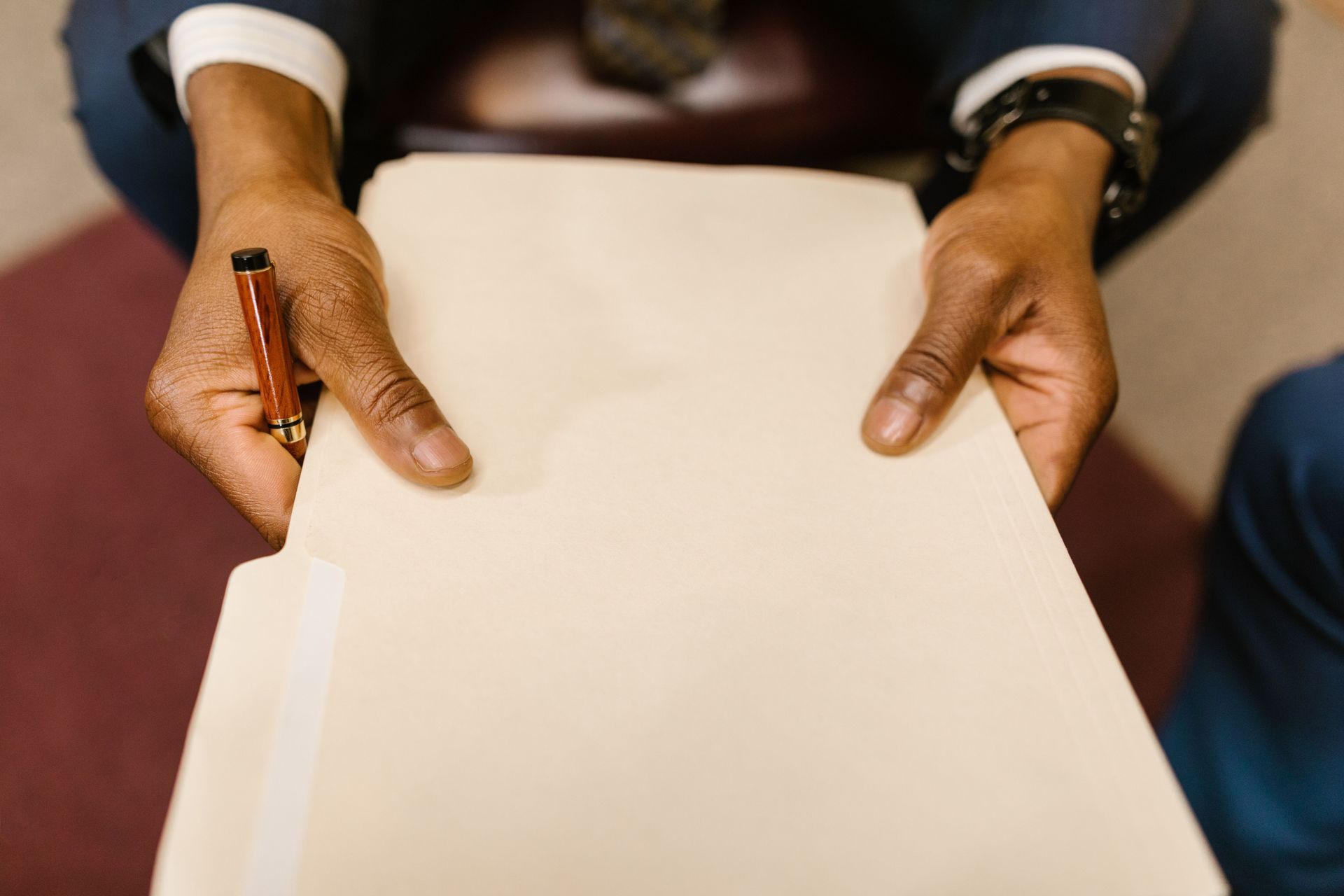 Hands holding a blank white sheet of paper with a pen on a table.