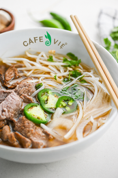 Bowl of clear noodle soup with white noodles, herbs, and sliced tofu on a light surface