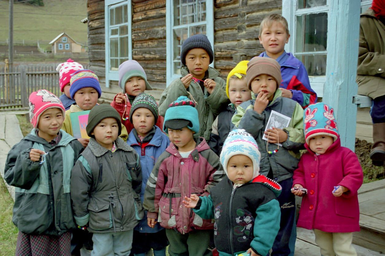 Group of children in colorful winter coats and hats standing outside a building