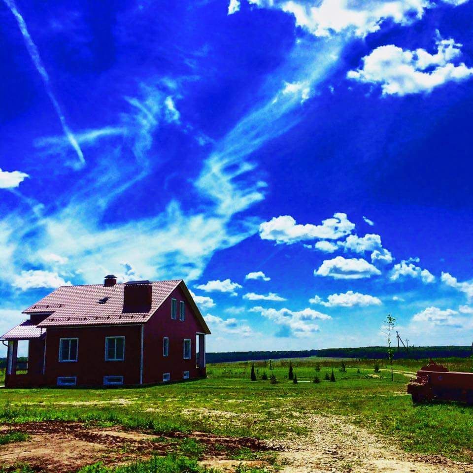 Red house in a grassy field under a vivid blue sky with clouds