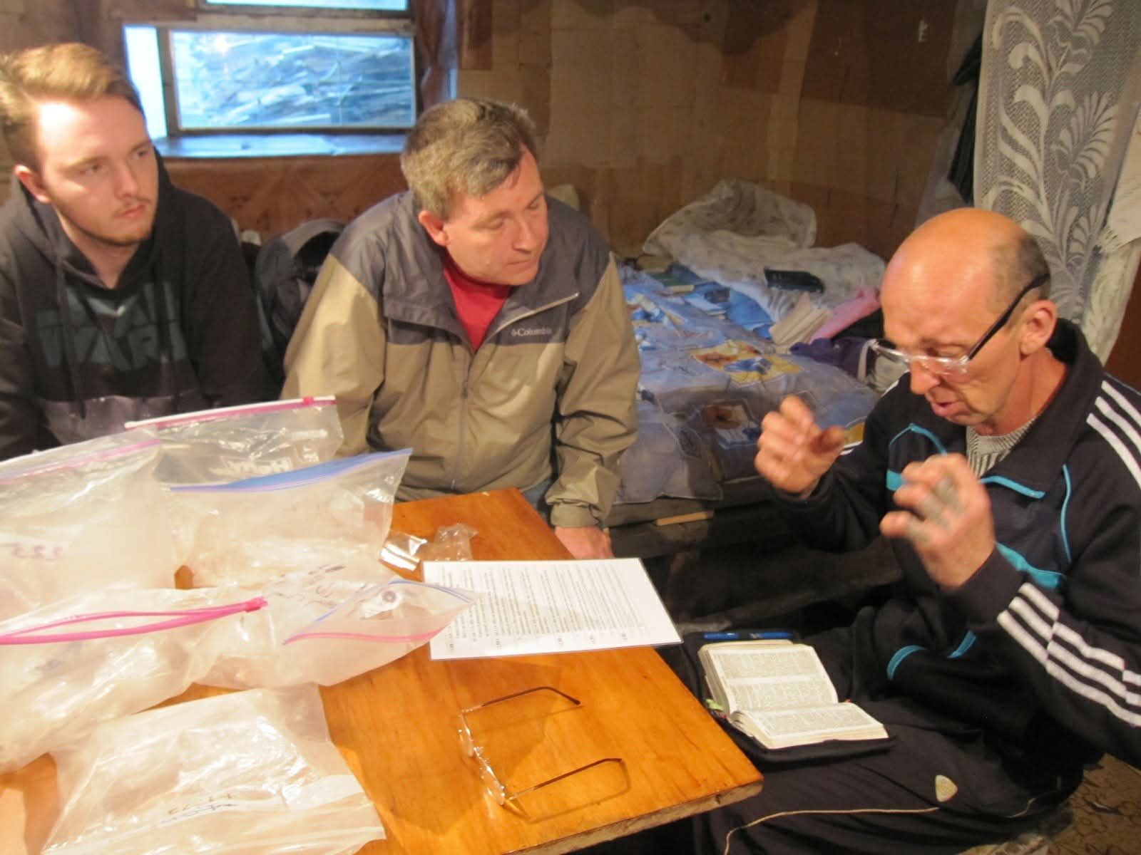 Three people sit at a table studying papers and a notebook in a wood-paneled room.