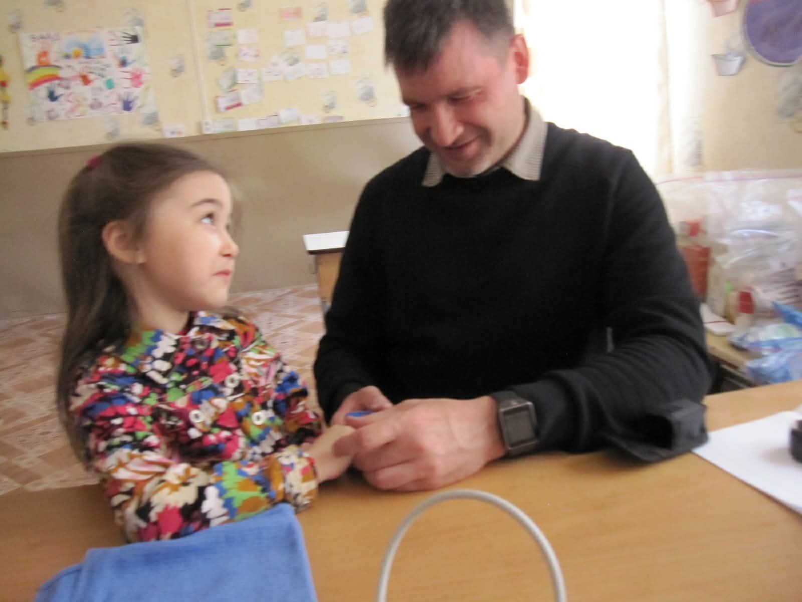 Adult and child seated at a table, holding hands and smiling in a classroom setting