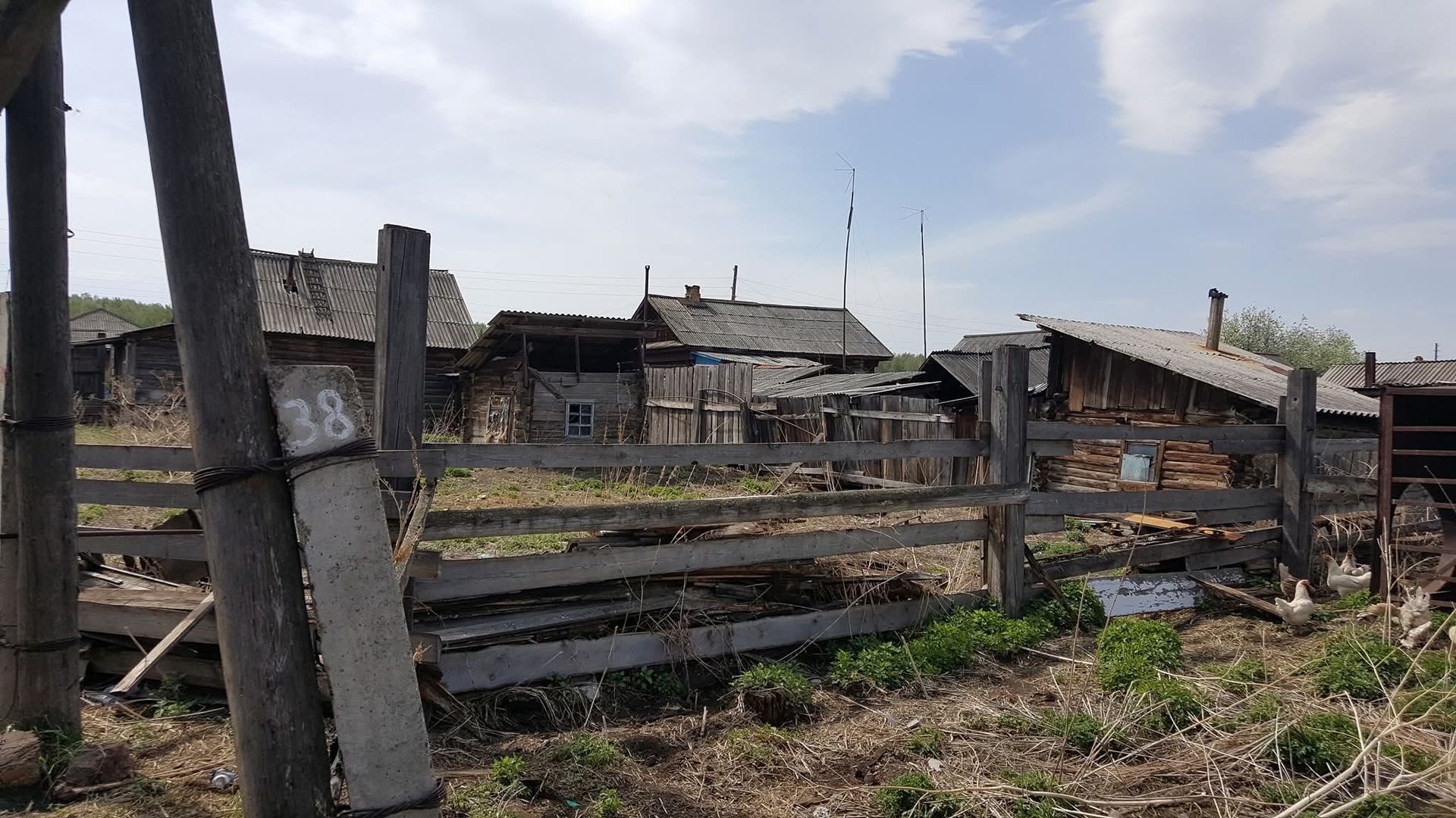 Rural yard with a weathered wooden fence and old buildings under a cloudy sky