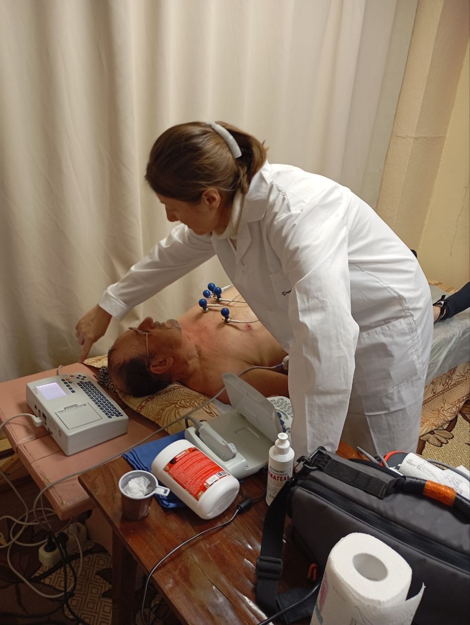 Medical worker performing CPR on a man lying on a table, with monitor and emergency equipment nearby